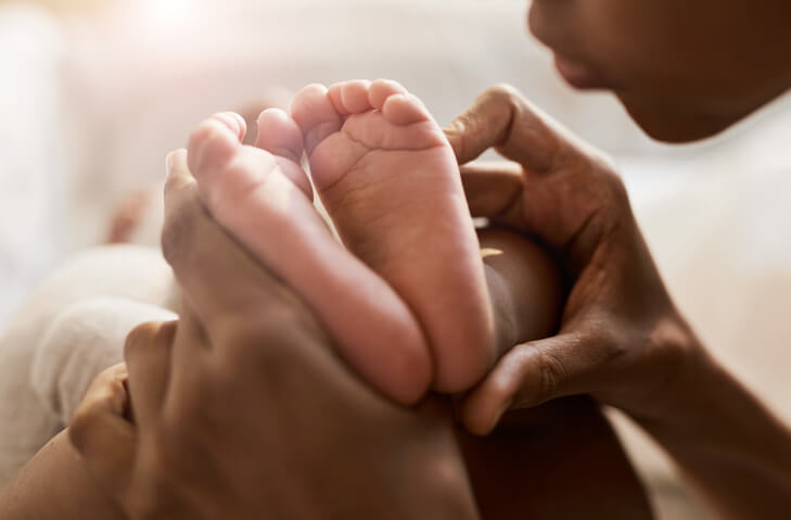 Close up portrait of African-American woman holding tiny feet of cute baby in sunlight
