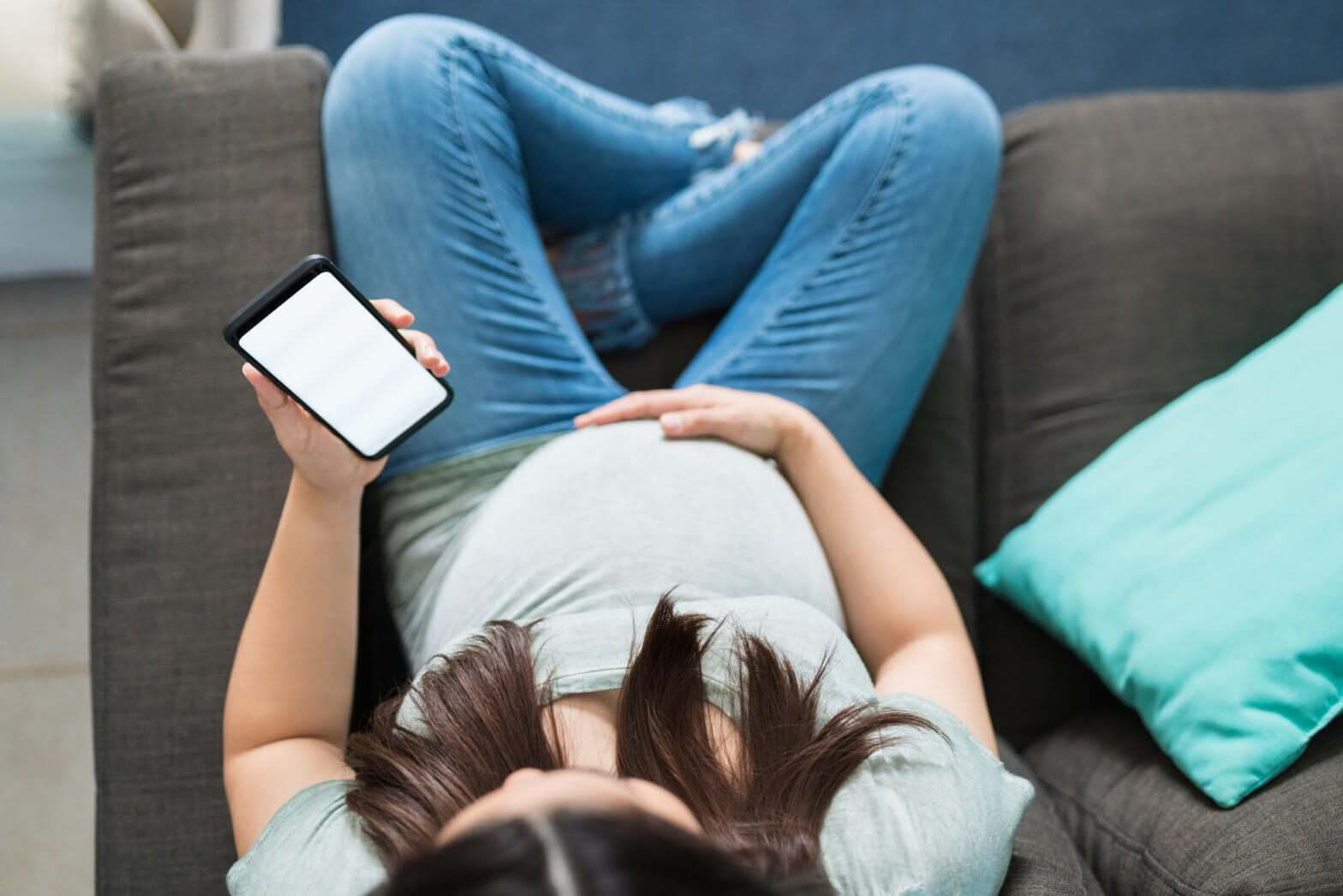 Caucasian pregnant woman relaxing while using smartphone in living room